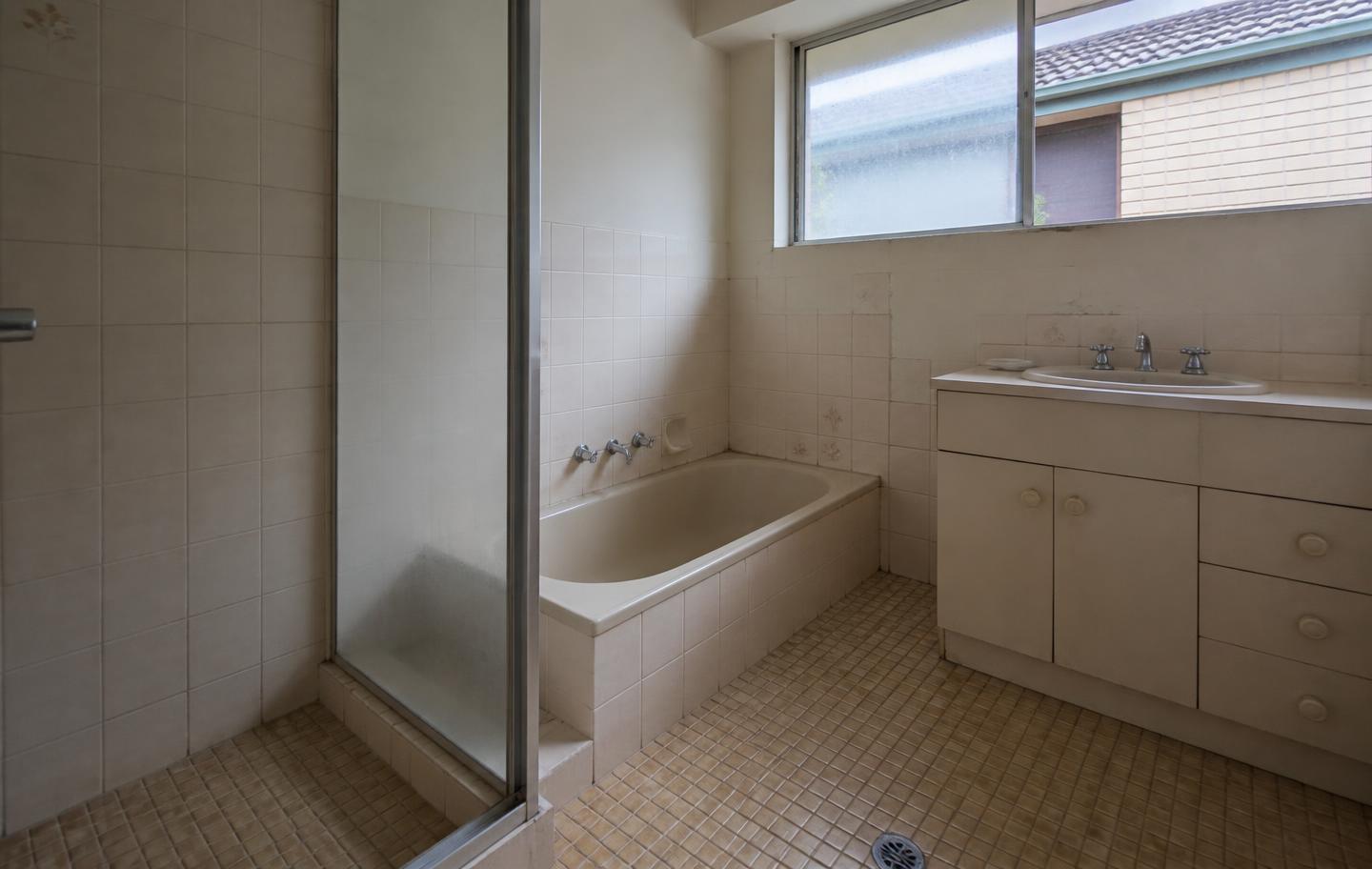 Tired beige tiled bathroom with dated vanity before renovation
